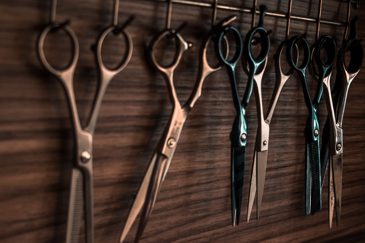 get-in-touch A collection of vintage barber scissors hanging on a wooden wall, showcasing sharp tools for hair cutting.